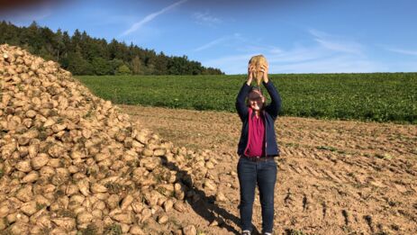 Beate Mayer hält eine große Bio-Zuckerrübe neben einem Berg von Zuckerrüben